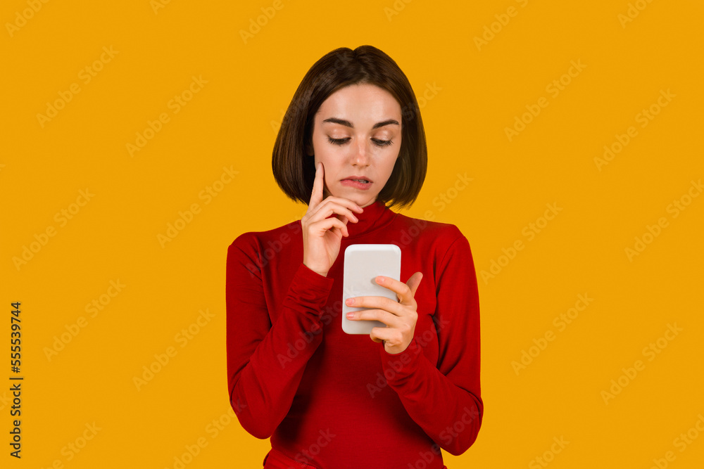 Curious attractive lady looking at cell phone screen, orange background Curious attractive lady looking at cell phone screen, orange background
