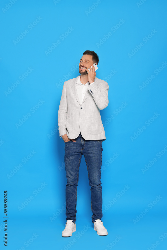 Handsome man talking on phone against light blue background Handsome man talking on phone against light blue background