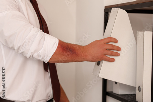 Man with bruise putting folder on shelf in office