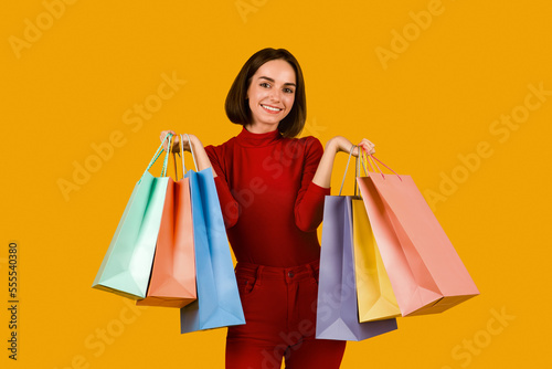 Happy pretty young woman holding colorful shopping bags on orange