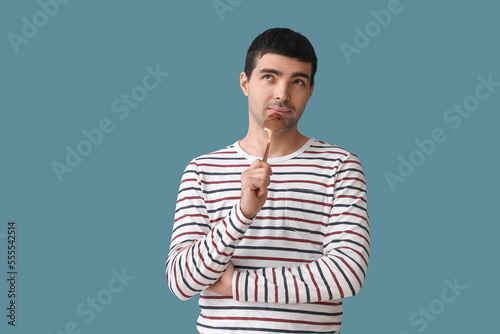 Thoughtful young man with golden spoon on color background