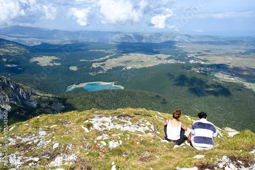 Hikers on the top of the mountain with the lake and forest beneath them.