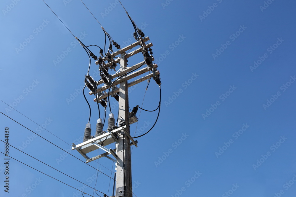Equipment with electric wires on poles. Recloser is a circuit breaker-like device located in a high-voltage power distribution system on a blue sky background with copy space and selective focus. Equipment with electric wires on poles. Recloser is a circuit breaker-like device located in a high-voltage power distribution system on a blue sky background with copy space and selective focus.