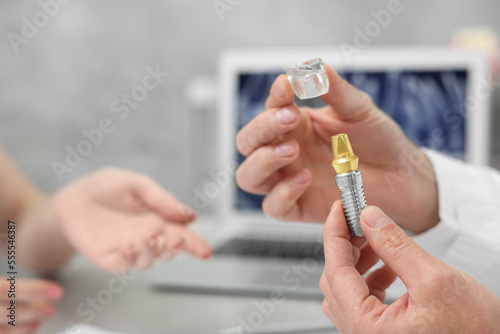 Doctor with educational model of dental implant consulting patient in clinic, closeup. Space for text