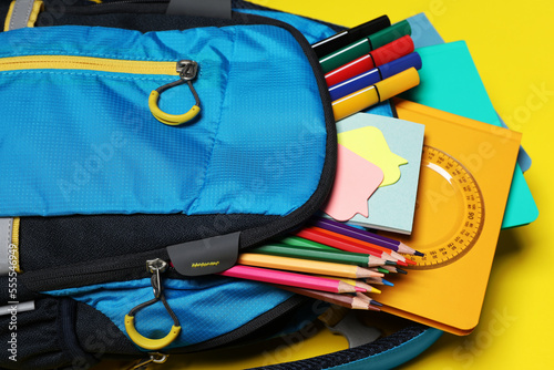 Backpack with school stationery on yellow background, closeup