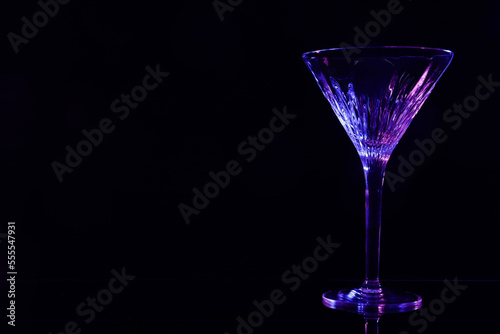 Beautiful martini glass on mirror table against black background. Space for text