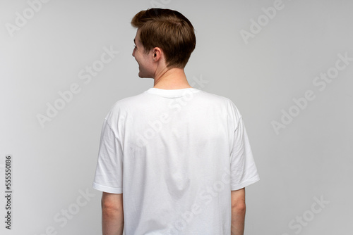 Back view of positive man looking away and smiling while posing back to the camera at studio
