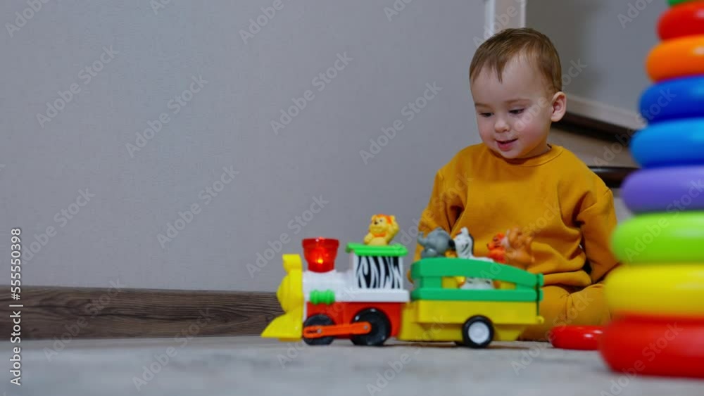 Cute toddler boy playing with colorful toy train on batteries. Little kid is jumping joyful from excitement. Cute toddler boy playing with colorful toy train on batteries. Little kid is jumping joyful from excitement.