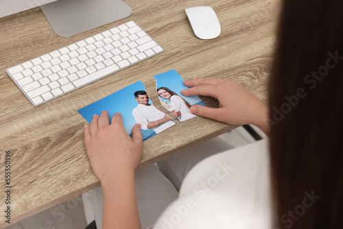 Woman holding torn photo at wooden table indoors, closeup. Divorce concept