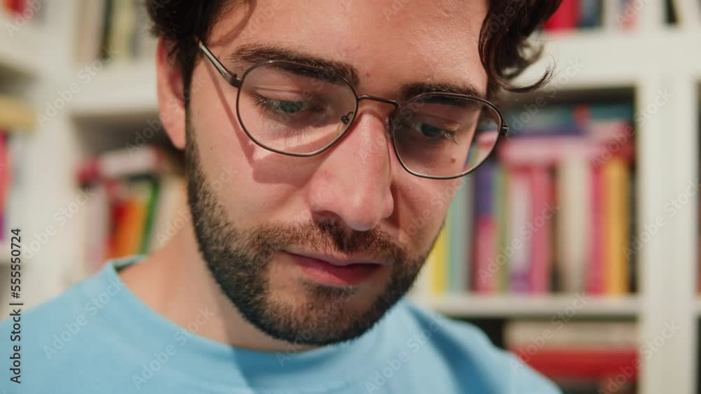 Man reading Book in University Library, Book Shop or Store, Spanish Student Wearing Glasses Standing near Bookshelf Reads Book and Exam Preparations. Man reading Book in University Library, Book Shop or Store, Spanish Student Wearing Glasses Standing near Bookshelf Reads Book and Exam Preparations.