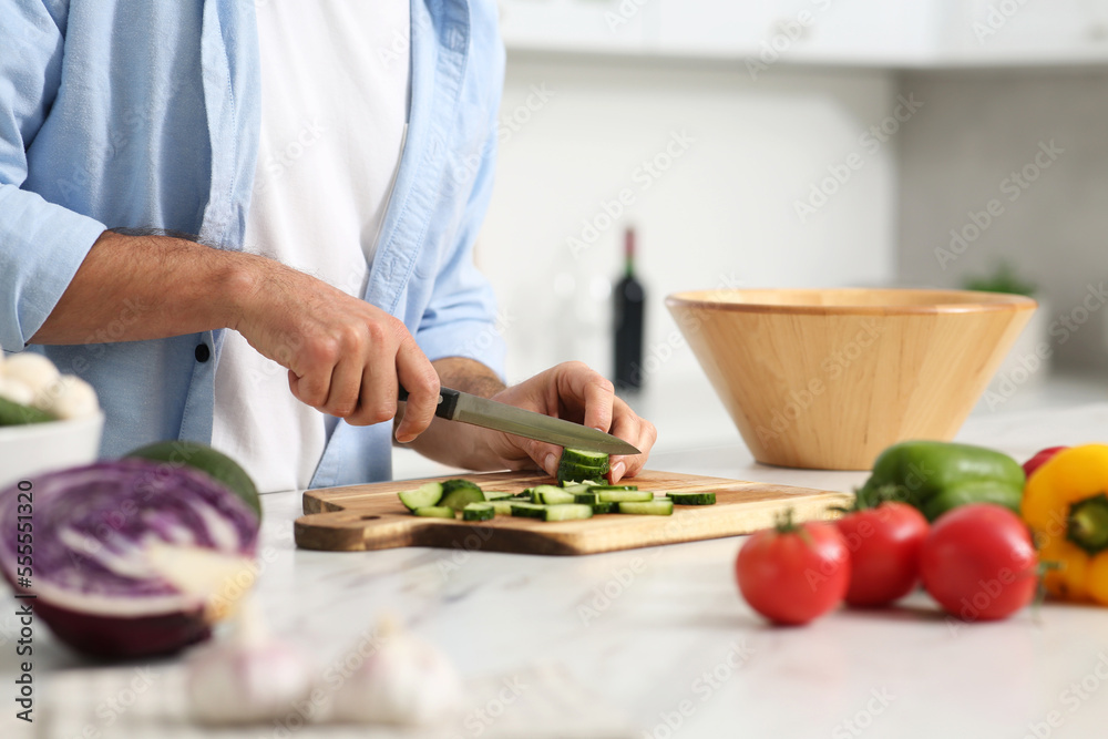 Man cutting cucumber at table in kitchen, closeup. Online cooking course Man cutting cucumber at table in kitchen, closeup. Online cooking course