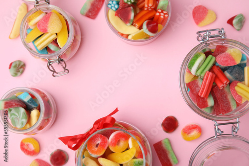 Frame made of glass jars with tasty colorful jelly candies on pink background  flat lay. Space for text