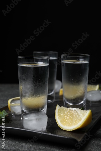 Shot glasses of vodka with lemon slices, mint and ice on grey table