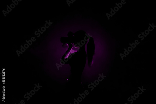 Center purple light silhouette on black background and lady photographer with camera taking photos. Concept of art photography. Dark violet picture for website, avatar, Surreal abstract backdrop