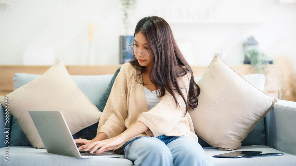 Young asian woman using laptop while seated on couch at home Young asian woman using laptop while seated on couch at home