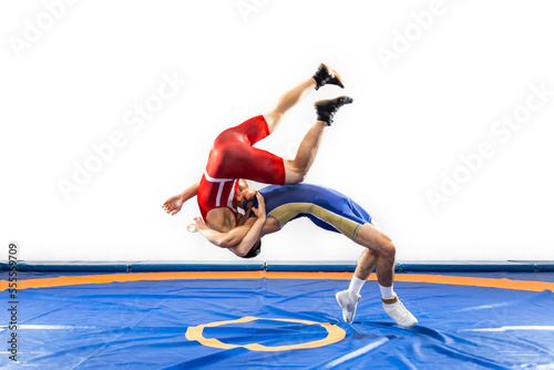 Two strong men in blue and red wrestling tights are wrestlng and making a suplex wrestling on a yellow wrestling carpet