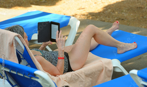 Woman relaxing on vacation, lying on a sunbed, reading from e-reader on a beach photo