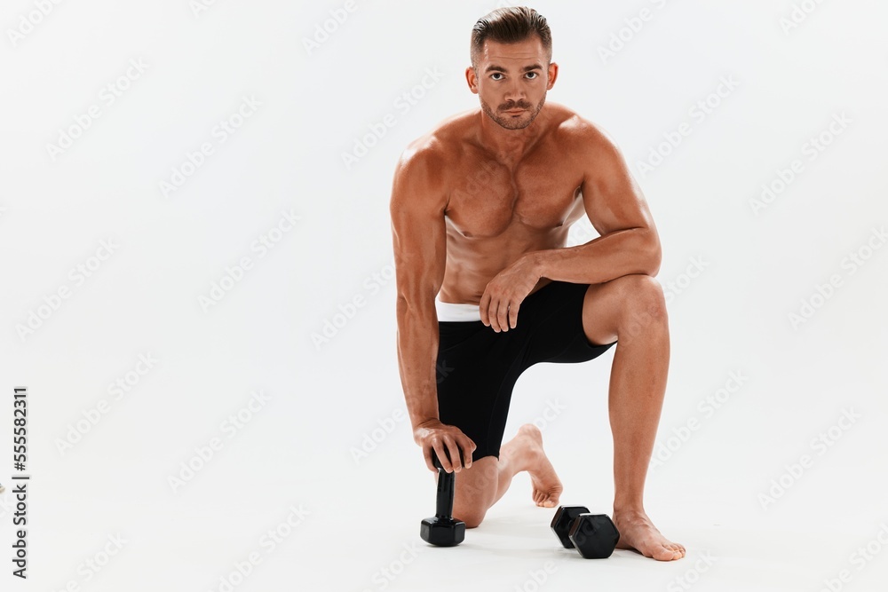 Man athletic body bodybuilder posing with dumbbells with naked torso abs full-length in the background, fitness class. Advertising, sports, active lifestyle, competition, challenge concept. Man athletic body bodybuilder posing with dumbbells with naked torso abs full-length in the background, fitness class. Advertising, sports, active lifestyle, competition, challenge concept.
