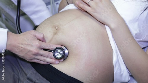 Doctor checks pregnant woman's belly with a stethoscope.