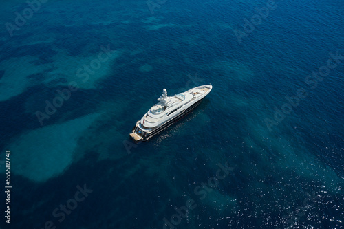 Big White Mega yacht is anchored on clear water, top view.