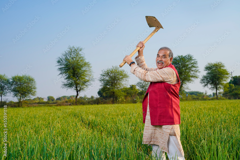 Indian farmer holding spade tool in hand and giving expression at agriculture field. Indian farmer holding spade tool in hand and giving expression at agriculture field.