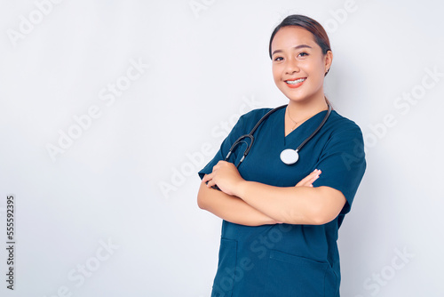 Smiling young Asian woman nurse wearing blue uniform with stethoscope cross arms chest and looking at the camera isolated on white background. Healthcare medicine concept