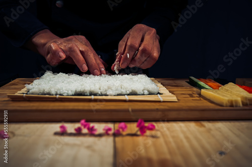 Japanese chef making California Maki Sushi with Masago - Roll made of Crab Meat, Avocado, Cucumber inside. Masago (smelt roe) outside with tuna, salmon, shrimp,traditional Japanese food ,Dark Tone