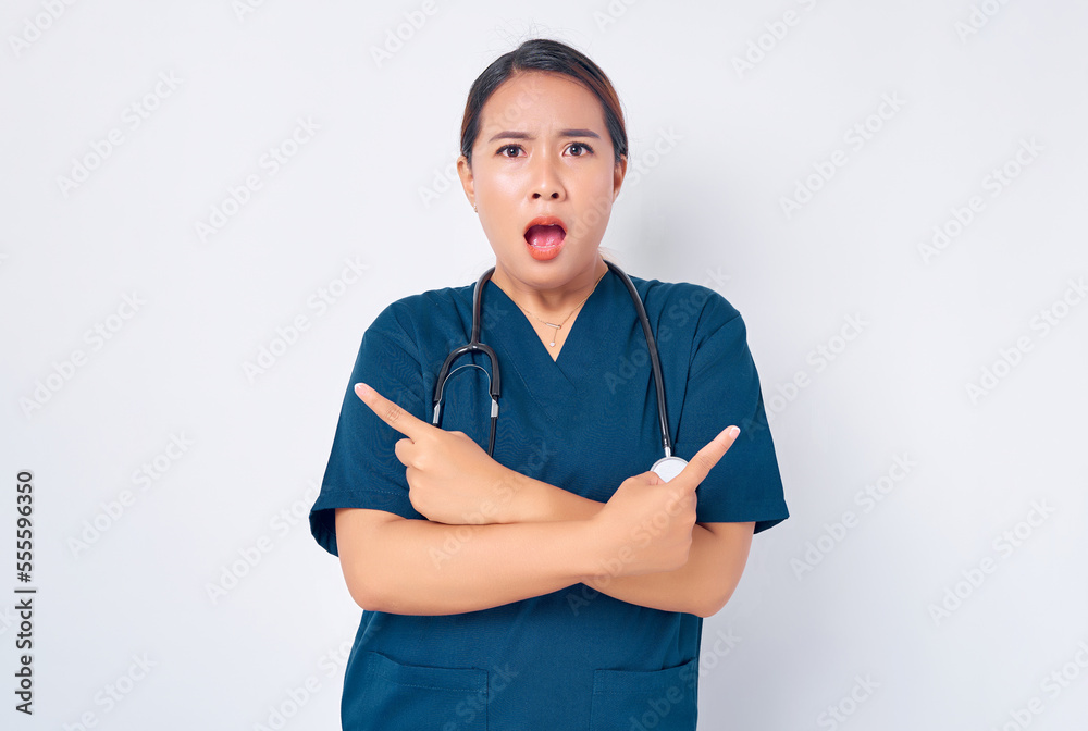Surprised Asian woman nurse wearing blue uniform with a stethoscope pointing fingers sideways left and right, showing two products or banners isolated on white background. Healthcare medicine concept Surprised Asian woman nurse wearing blue uniform with a stethoscope pointing fingers sideways left and right, showing two products or banners isolated on white background. Healthcare medicine concept