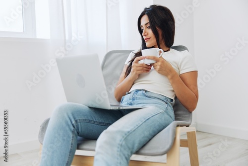 Woman relaxing at home sitting on a chair and watching a movie on her laptop with a cup of tea, smile autumnal mood