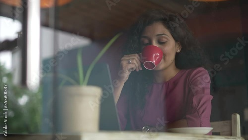 beautiful Young Indian woman is sitting comfortably sipping coffee in a cafe.Charming young Asian female drinking hot coffee or tea sitting at table looking on window. photo