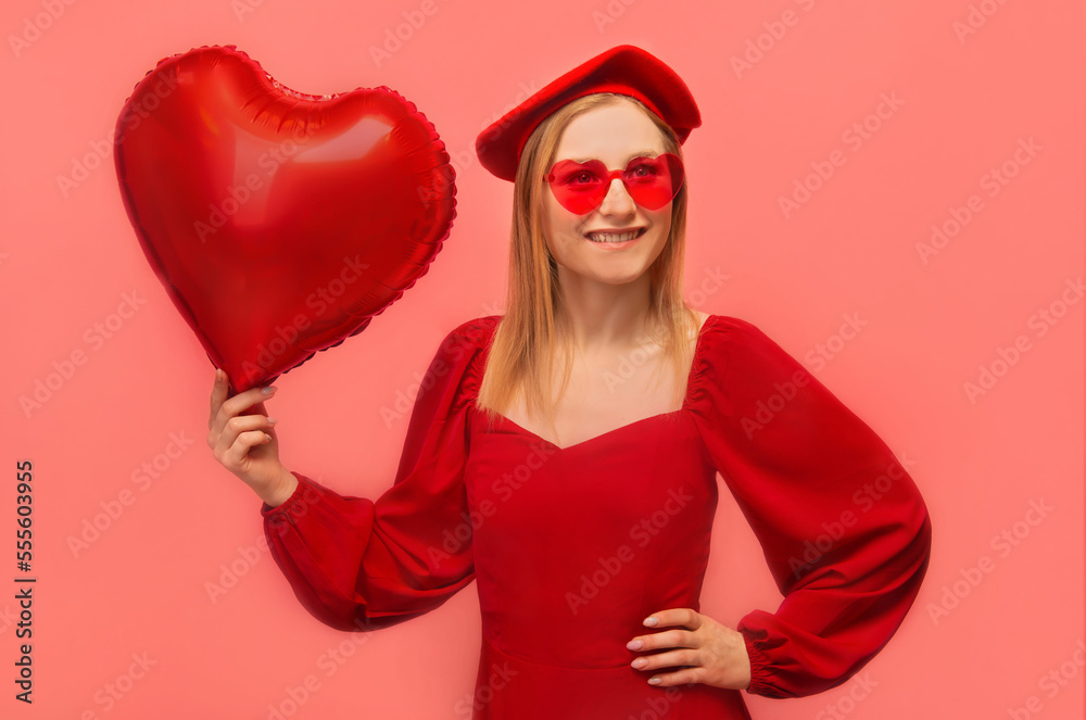 Happy smiling stylish girl holding red heart shaped air balloon, wearing red dress with sleeves, french beret with trendy heart shaped glasses, keep hand on hip and looking up on pink background. Happy smiling stylish girl holding red heart shaped air balloon, wearing red dress with sleeves, french beret with trendy heart shaped glasses, keep hand on hip and looking up on pink background.