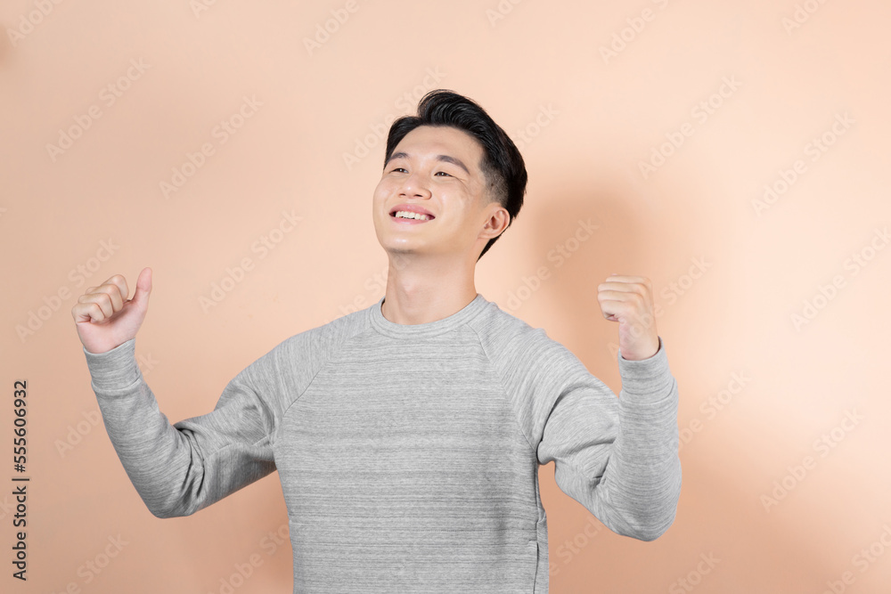 Young Asian man showing fist and happy sign isolated on beige background. Young Asian man showing fist and happy sign isolated on beige background.