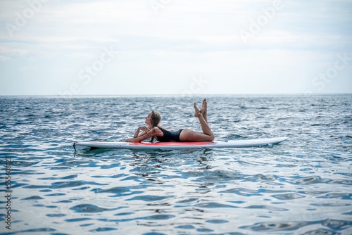 Woman sap sea. Sports girl on a surfboard in the sea on a sunny summer day. In a black bathing suit, he lies on a sap in the sea. Rest on the sea. © svetograph