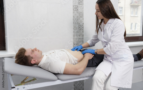 Fotografie A focused young woman doctor conducting abdominal palpation in a middle-aged pat