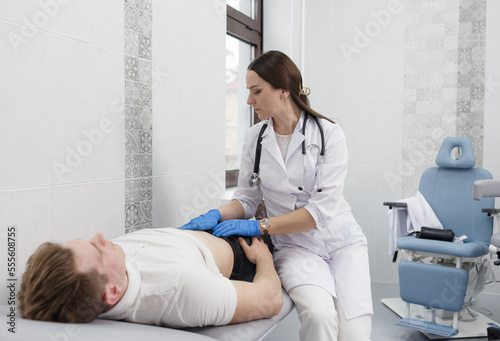A focused young woman doctor conducting abdominal palpation in a middle-aged patient suffering from pain young man