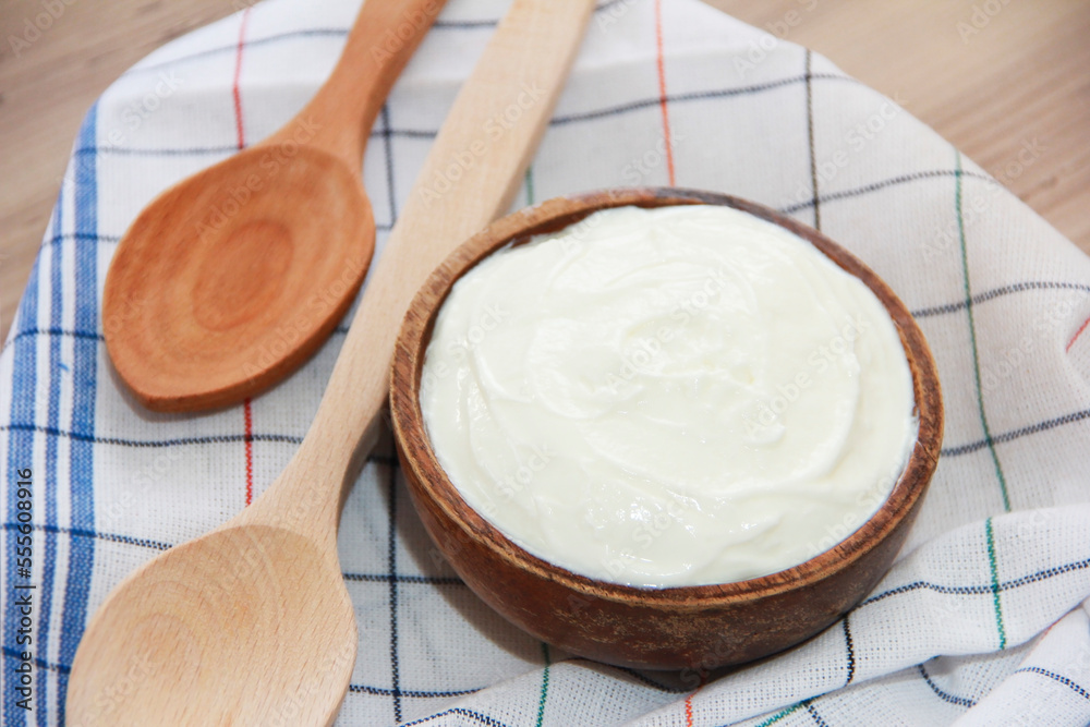 White fermented milk yogurt in a decorative plate and wooden spoons on a brown background White fermented milk yogurt in a decorative plate and wooden spoons on a brown background