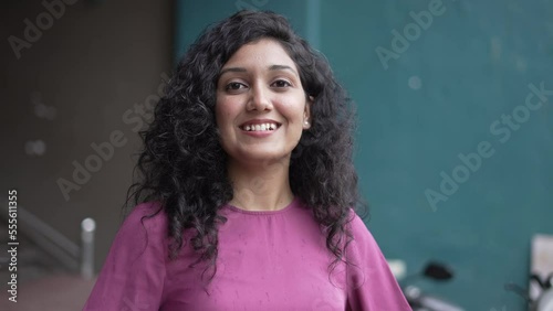 Beautiful smiling confident young Indian woman pretty face looking at camera posing alone at standing in the parking. happy millennial Hindu ethnicity girl student professional close up front portrait