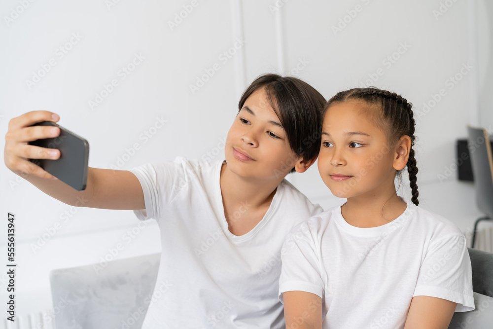 Preteen asian boy taking selfie on cellphone with sister at home Preteen asian boy taking selfie on cellphone with sister at home