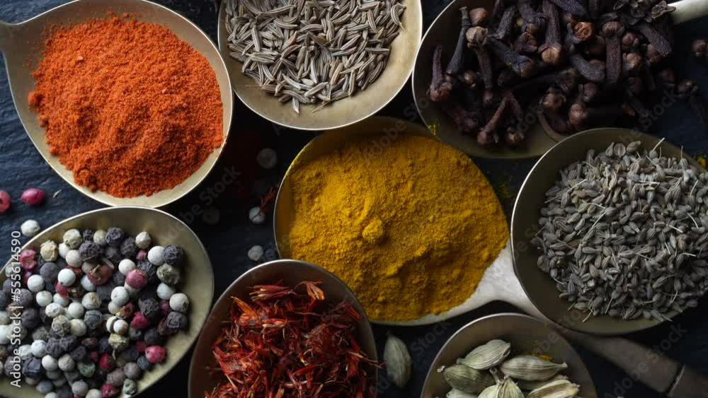 Set of spices in brass spoons, rotates, close up, top view. Various peppers, cardamom, carnation, turmeric, paprika and saffron for cooking