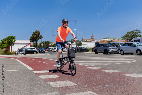 signore anziano con caschetto di protezione pedala sulla su bici  bici elettrica lunga la pista ciclabile in un percorso urbano. photo