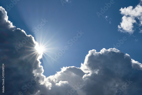 the sun rising from behind the clouds forming a solar star and the blue sky in the background