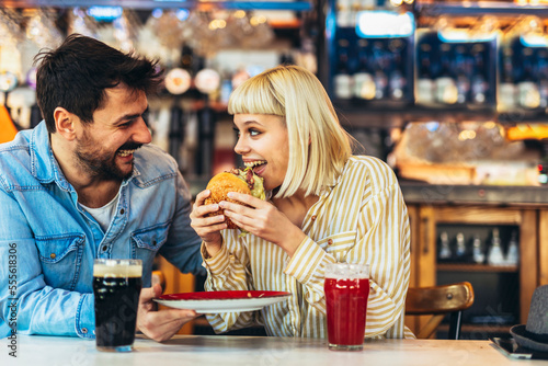 Young couple in love having fun spending leisure time together at restaurant, eating burgers and drinking beer