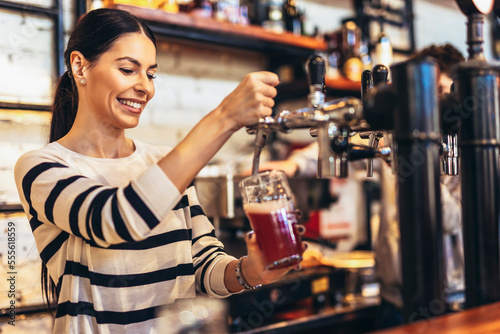 Female bartender tapping beer in bar.