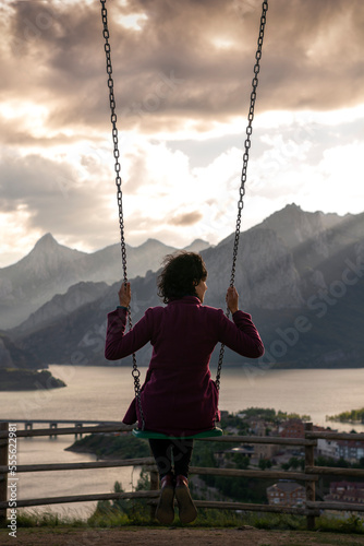 A young Woman is looking the lake and village of Riaño swinging in the top of the mountain