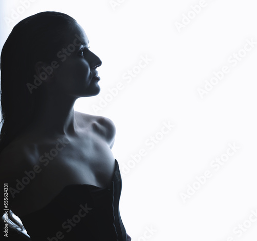 Portrait of beautiful and sexy brunette woman silhouette with black corset and wet hair in glowing studio background. Model standing in grace pose and looking aside camera. Toned image with blue color