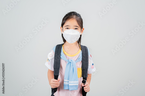 Asian little child girl carry a backpack wearing respirator mask to protect coronavirus outbreak and pointing hand to blank background  New virus Covid-19