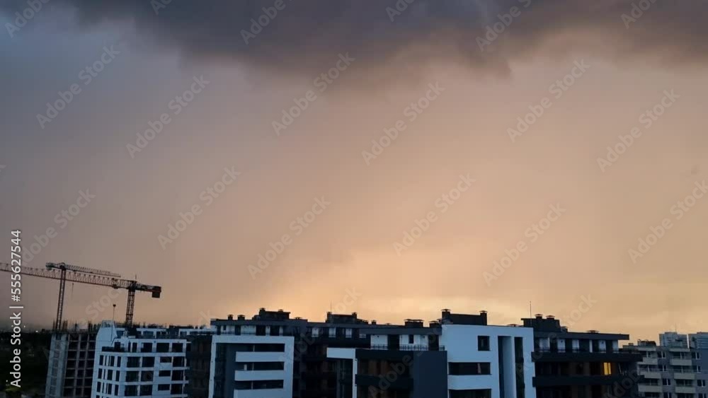 Night thunderstorm with illuminated cloudy sky with lightning over buildings and cityscape Night thunderstorm with illuminated cloudy sky with lightning over buildings and cityscape
