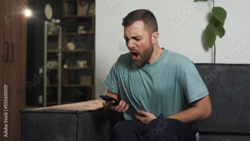 Portrait of a young man suffering from a sharp stomach ache while sitting on a sofa photo