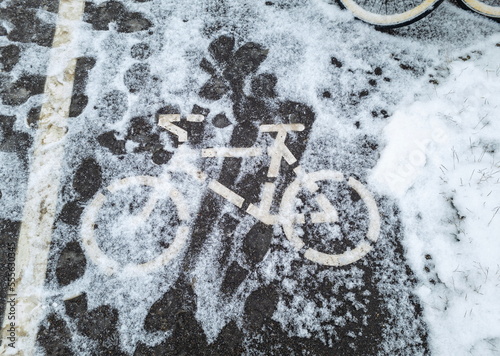 The sign of the bike path on the asphalt covered with fallen snow. Winter weather in Europe.
