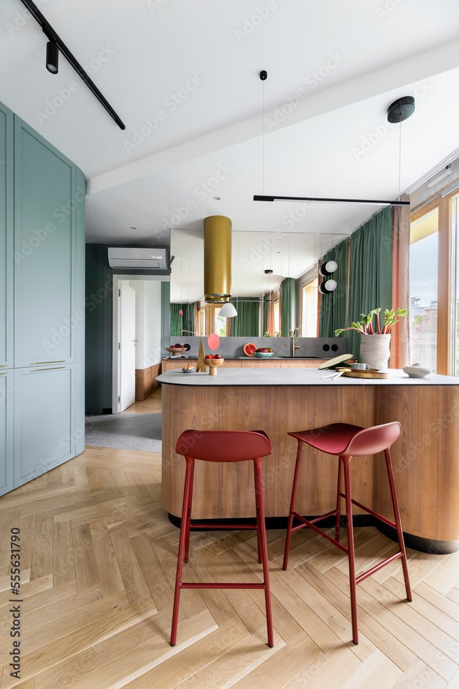 Modern composition of kitchen interior with wooden kitchen island, red  barstools, colorful sculpture, green curtain, gold cooker hood, vase with  rhubarb and personal accessories. Home decor. Template. Photos | Adobe Stock